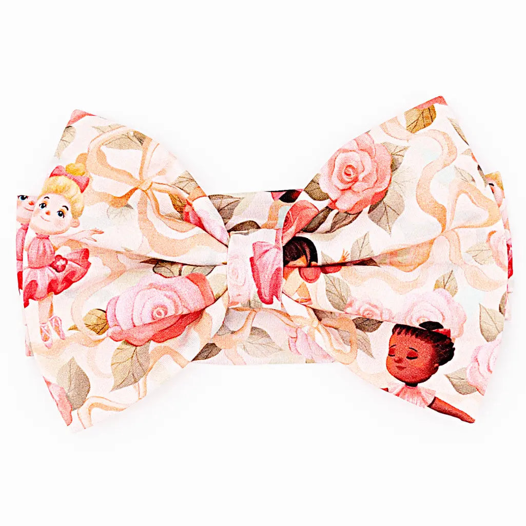 Close-up of a bow headband printed with pink roses, ribbons, and little ballerinas on a white background.
